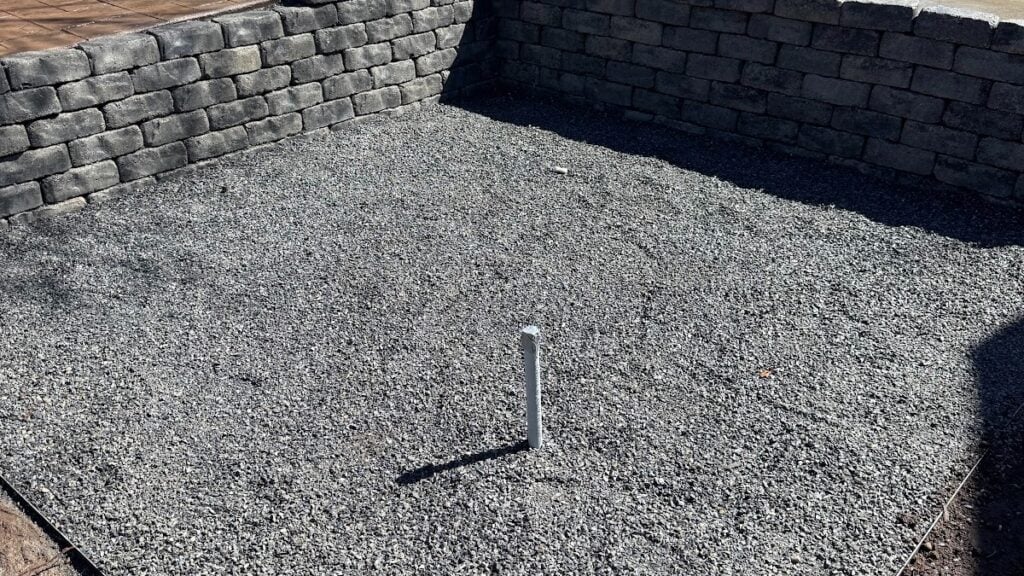 A gravel-filled area bordered by stone retaining walls, with a single white PVC pipe sticking up from the center, showcases the clean and functional aesthetic often seen in professional landscape design services throughout West Jordan, Utah.