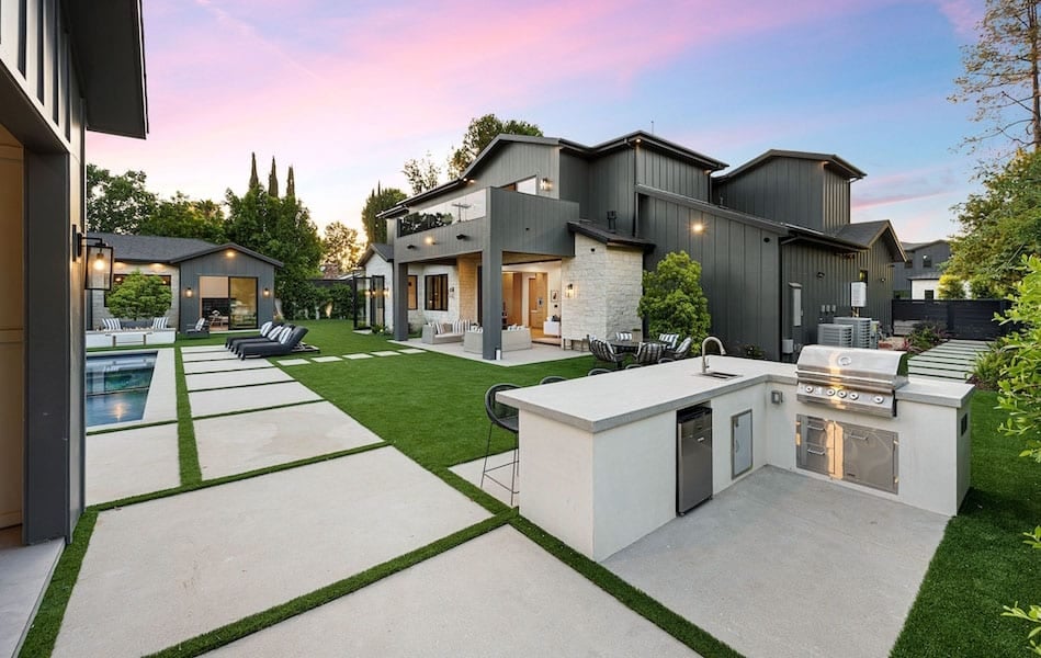Modern backyard featured on the homepage, with outdoor kitchen, built-in grill, seating area, pool, and contemporary house surrounded by landscaped greenery at sunset.