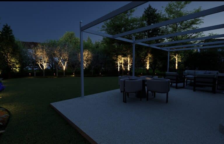 A backyard patio featuring a pergola and outdoor dining furniture, accented by illuminated trees under low voltage landscape lighting at night.