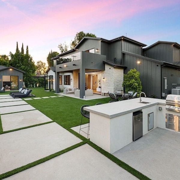 Modern backyard featured on the homepage, with outdoor kitchen, built-in grill, seating area, pool, and contemporary house surrounded by landscaped greenery at sunset.
