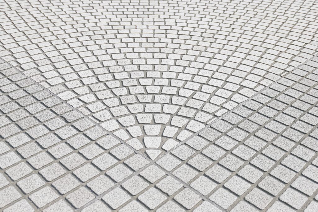 Geometric pattern of small, light-colored square tiles arranged in a fan or radial design on a paved surface, perfect for elegant paver driveways and professional driveway installation.